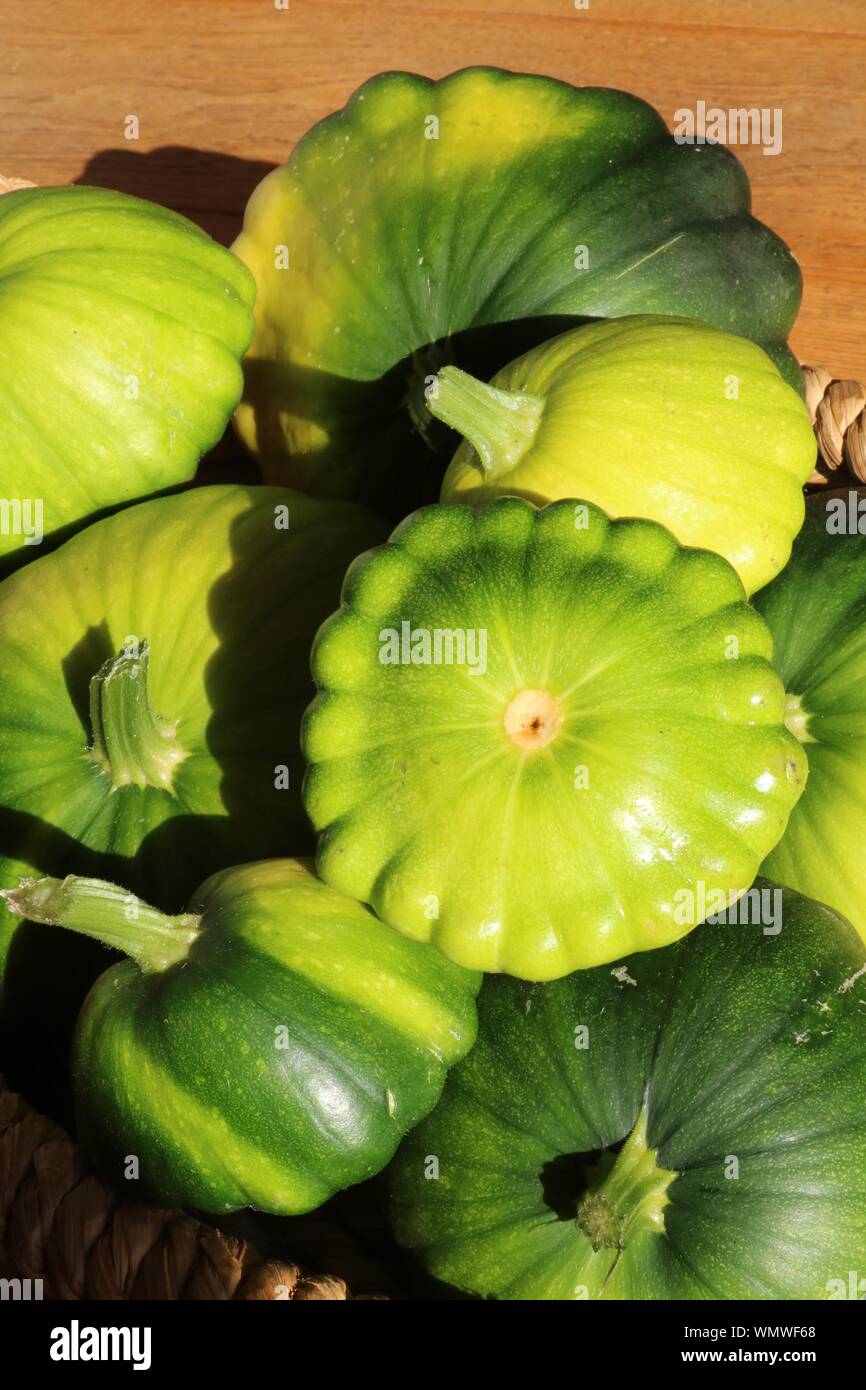 Green Patty pan smerlo refilato zucche di varie dimensioni in un basked al sole con pavimenti in rovere in background Foto Stock