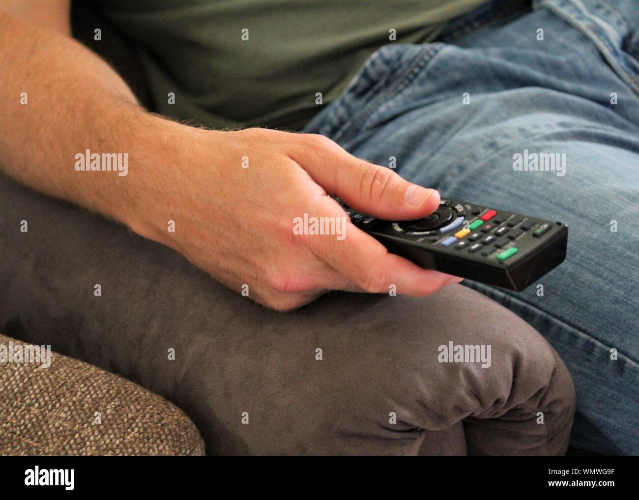 Una chiusura di una mano di un uomo utilizzando il telecomando di un televisore mentre è seduto in poltrona Foto Stock