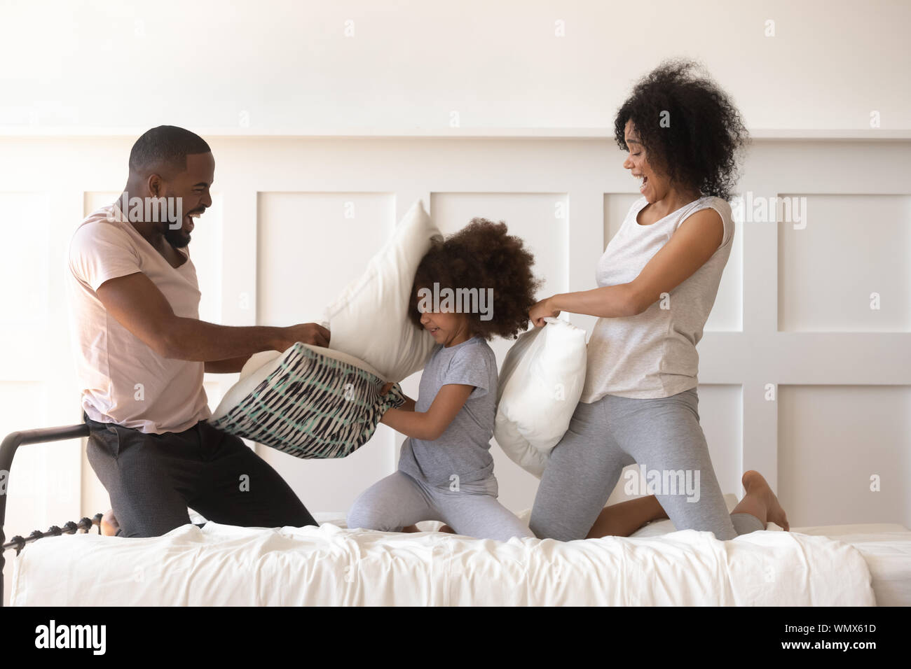 Felice famiglia americana africana in lotta con cuscini sul letto. Foto Stock