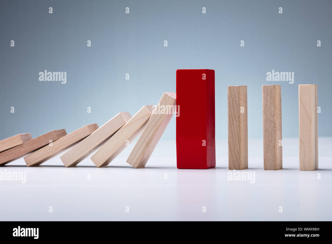 Close-up di rosso il blocco di legno tra la caduta e il montante Domino pezzi sulla superficie bianca Foto Stock