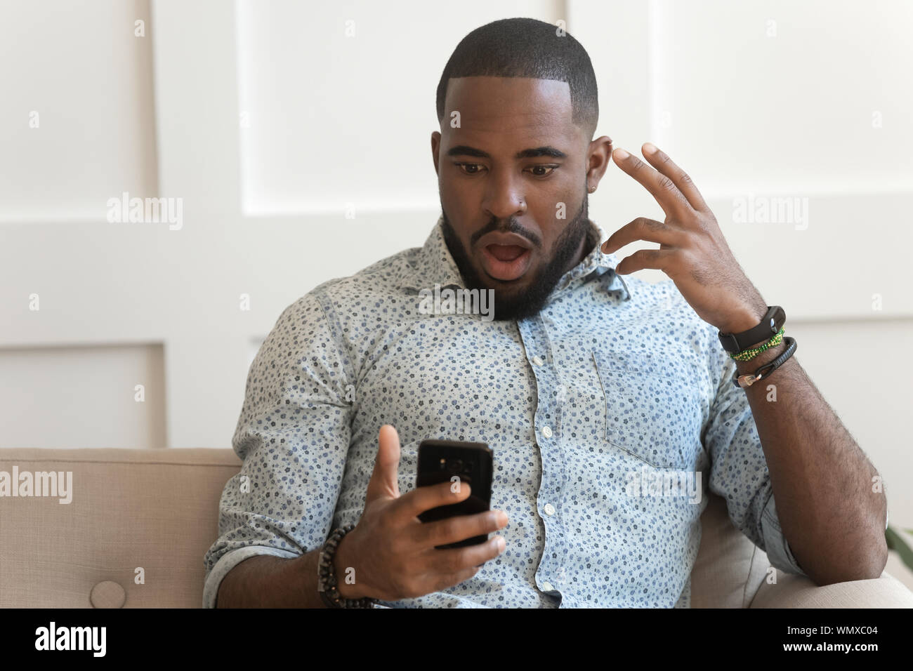 Scioccato la millenaria African American Uomo con telefono. Foto Stock