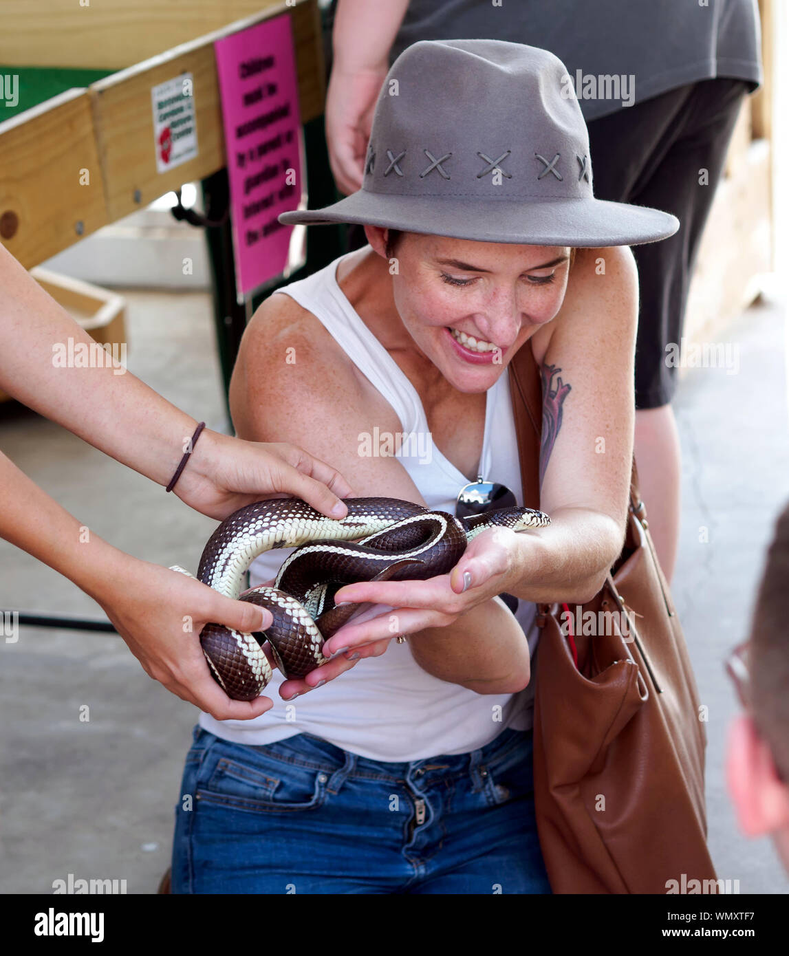 Sorridente donna caucasica nel cappello e il serbatoio superiore accetta un California kingsnake offerto al 2019 Arts Festival viva. Il Corpus Christi, Texas USA. Foto Stock