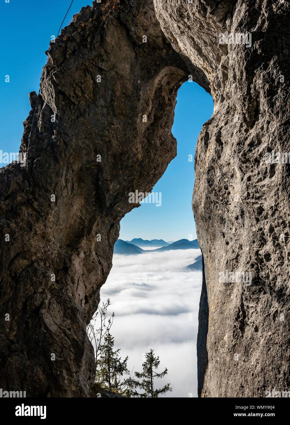 Visualizzazione attraverso l'arco naturale Breitensteinfensterl alla nebbia alta sopra la valle, sentiero escursionistico di Breitenstein, Fischbachau, Baviera, Germania Foto Stock