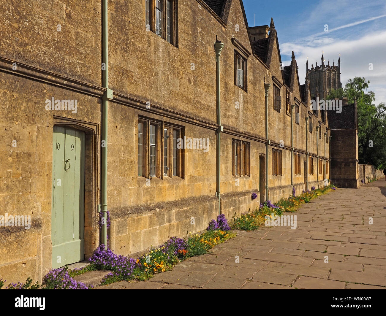 Il campanile della chiesa oltre la facciata del vecchio gli ospizi di carità nei caratteristici locali golden color miele pietra di Cotswold in Chipping Campden, Gloucestershire,l'Inghilterra, Regno Unito Foto Stock