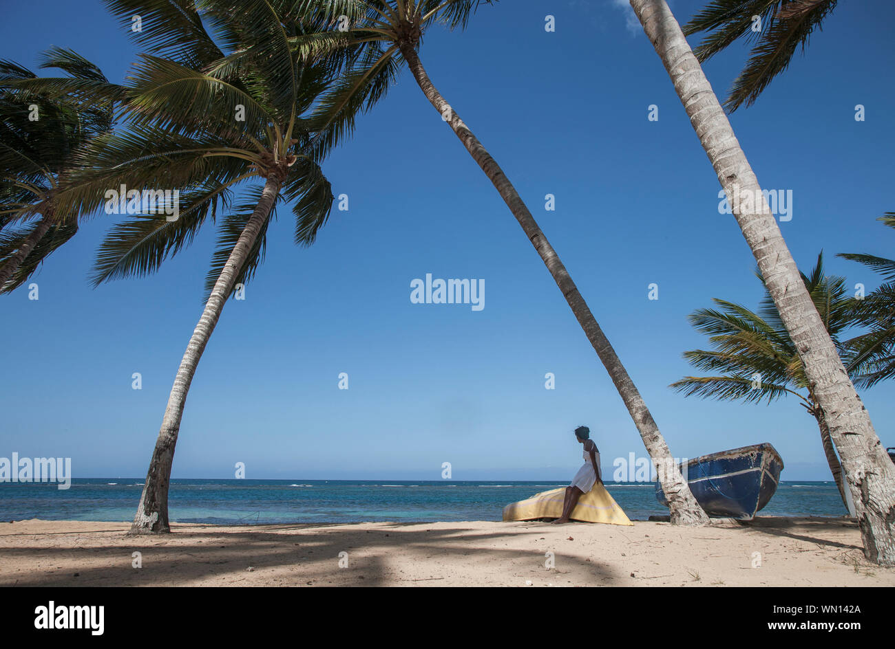 Donna seduta sulla barca sotto le palme sulla spiaggia in Las Terrenas Repubblica Dominicana Foto Stock