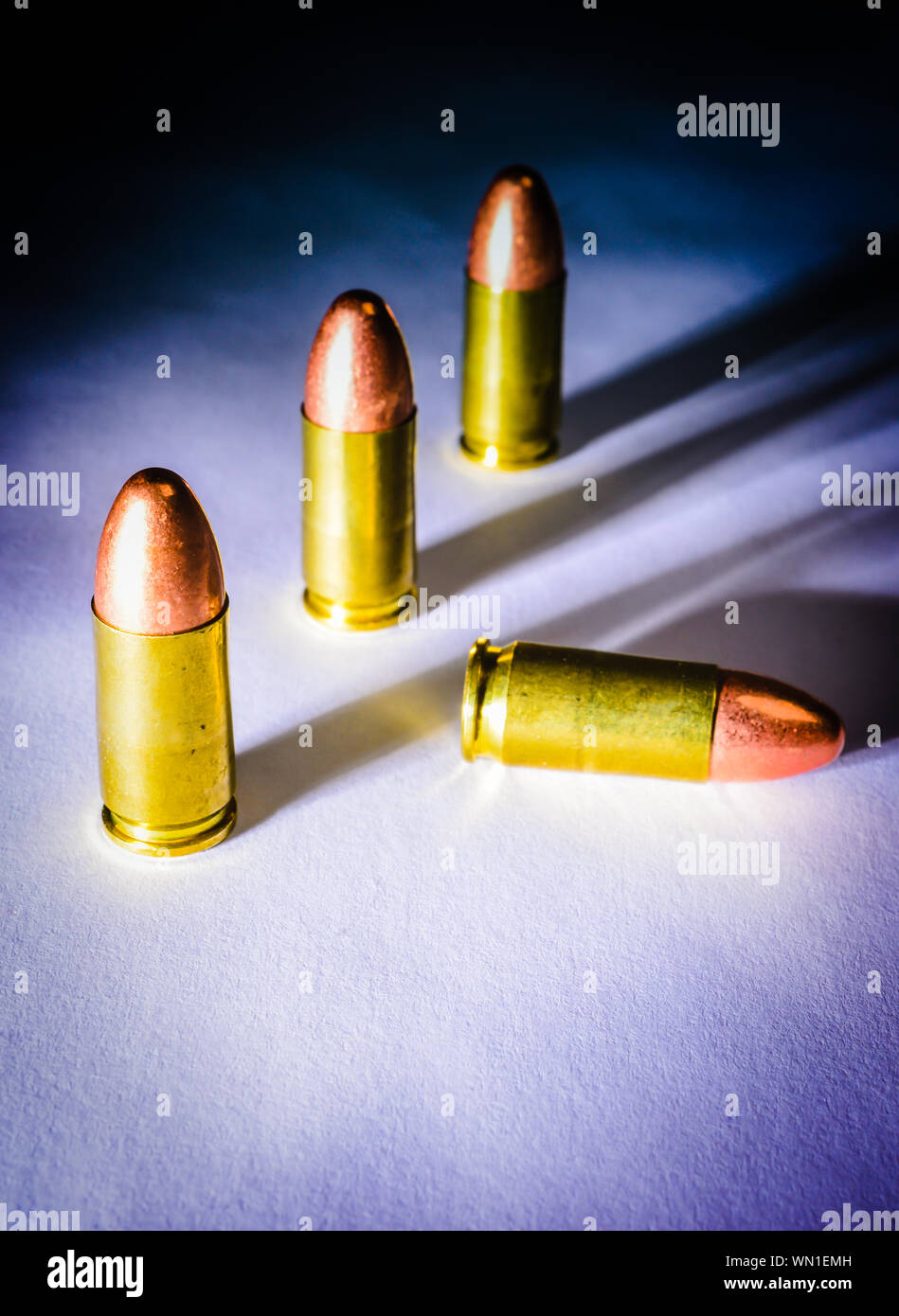 Tre piedi 9mm proiettili a fianco di un caduto bullet con drammatica luce laterale, ombre e colore Foto Stock