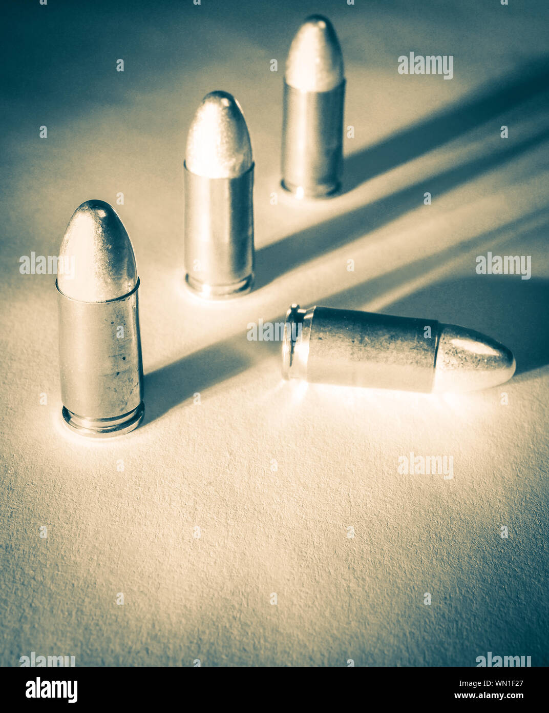 Tre piedi 9mm proiettili a fianco di un caduto bullet con lato drammatico di luce e le ombre in un tono di platino Foto Stock