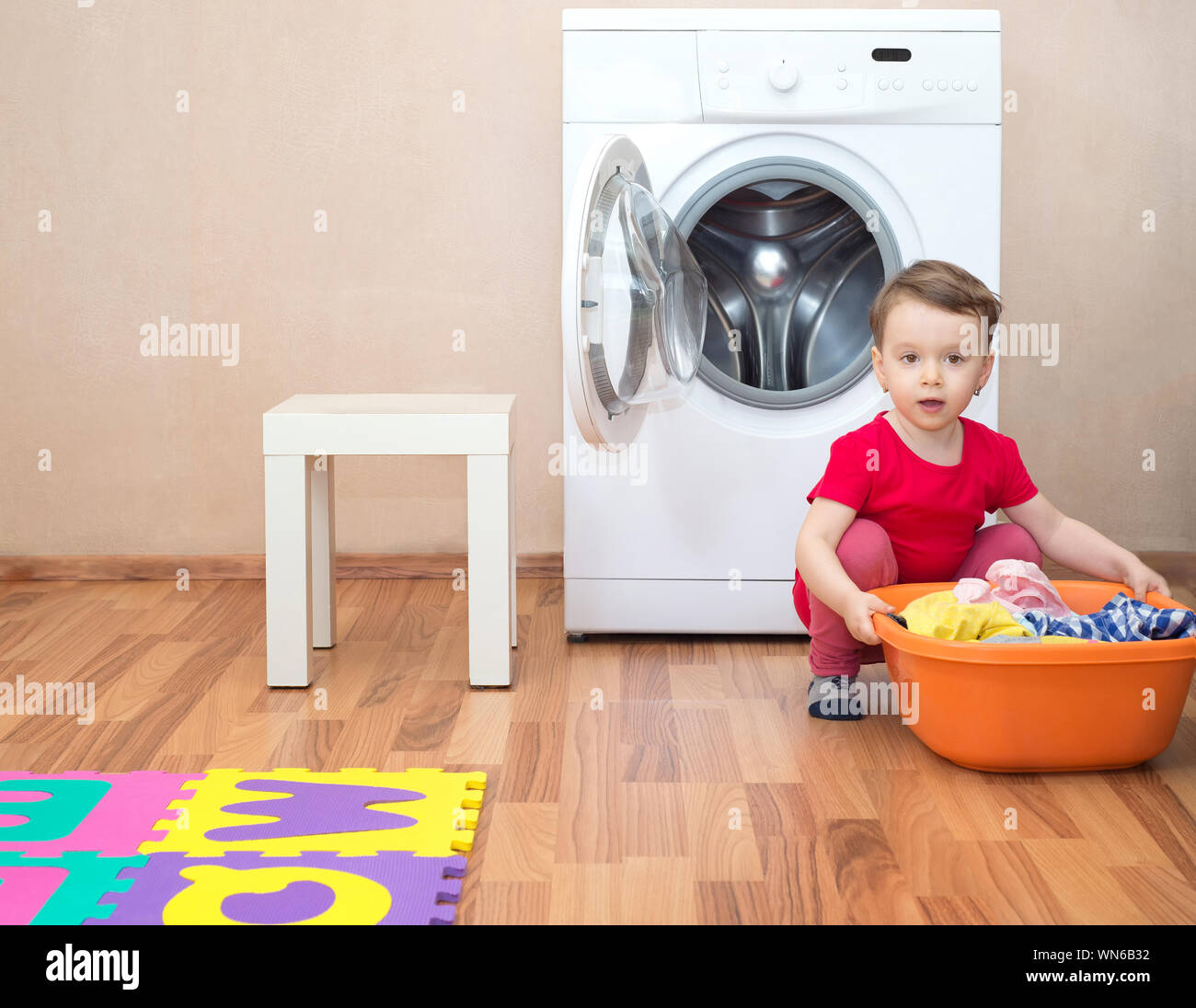 Bambina con un una bacinella piena di vestiti nella parte anteriore della macchina di lavaggio Foto Stock