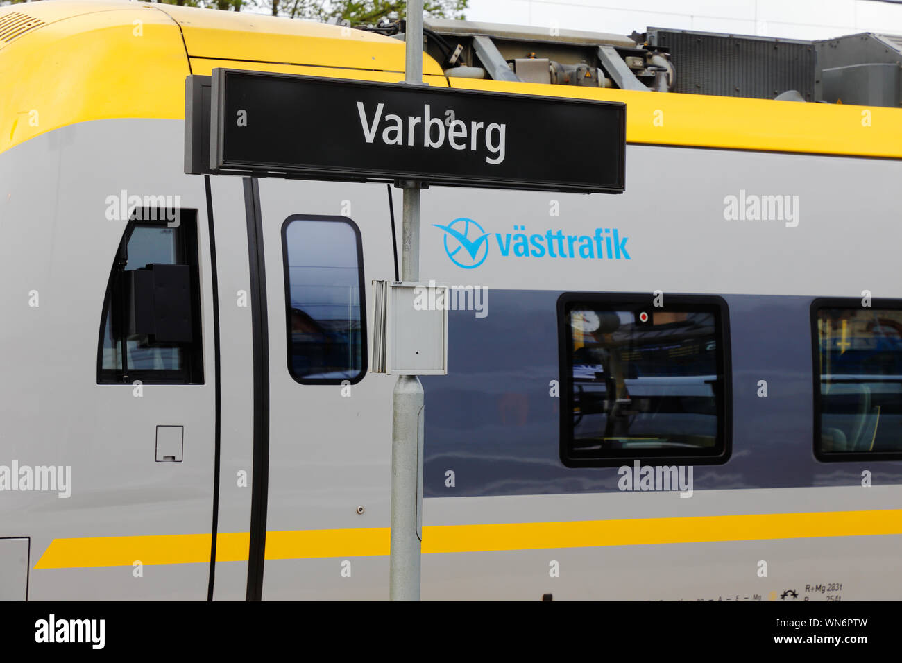 Varberg, Svezia - 3 Settembre 2019: Il Varberg railroad station segno davanti di un treno dei pendolari in servizio per Vasttrafik. Foto Stock