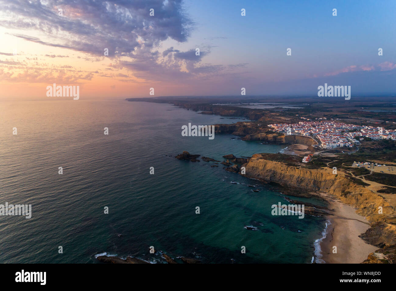Vista aerea del Zambujeira do Mar villaggio e la spiaggia al tramonto, in Alentejo, Portogallo; Foto Stock