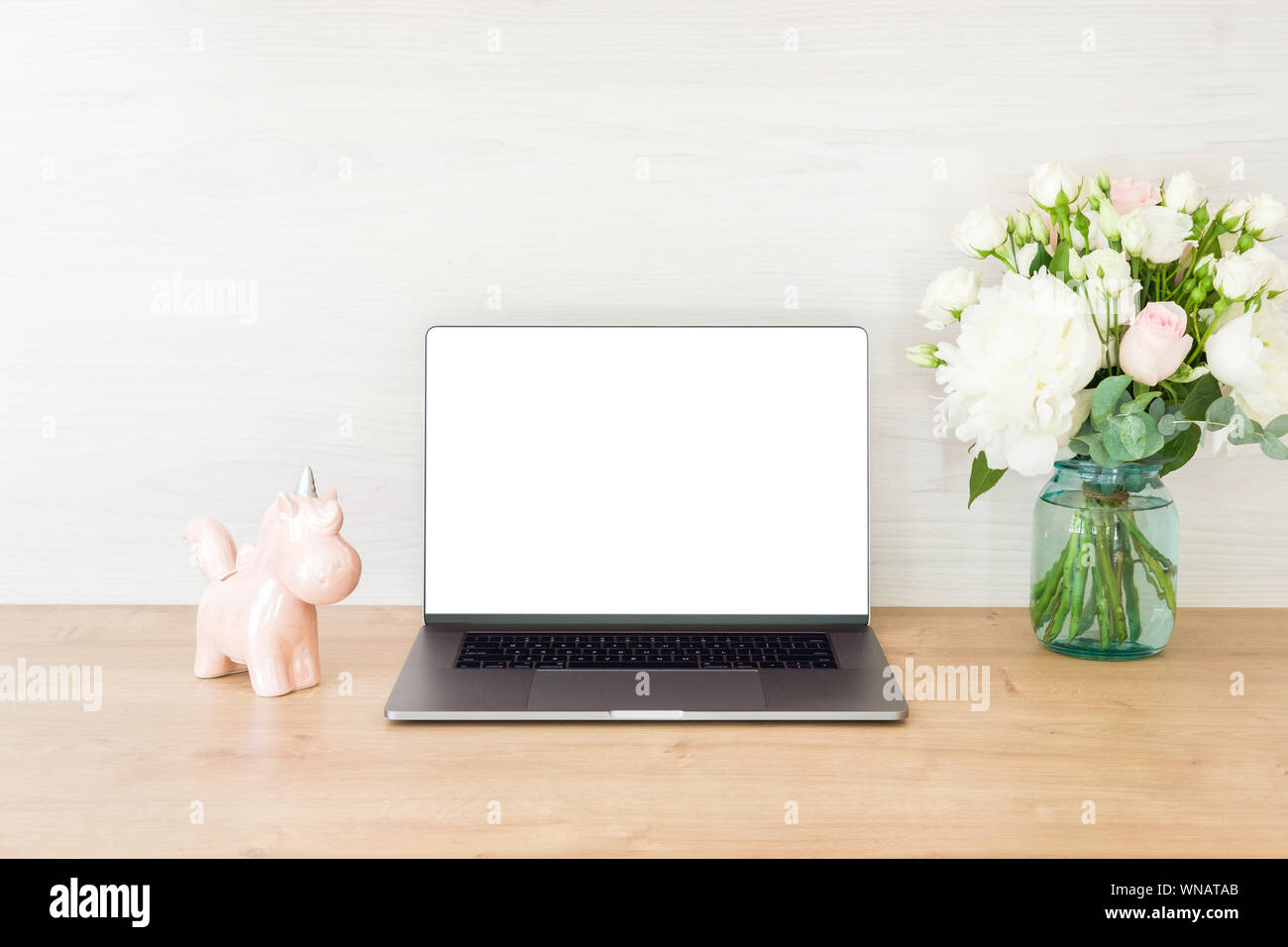 Computer portatile con schermata bianca vuota, Unicorn, bouquet di fiori su Office Workplace. Femminile home office desk tabella. Area di lavoro elegante mock up. Foto Stock
