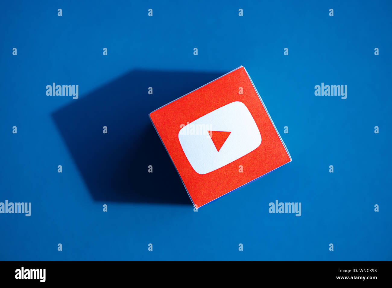 Un colpo dal di sopra del cubo di carta con il logo stampato dell'applicazione YouTube, che posto su uno sfondo blu. Foto Stock