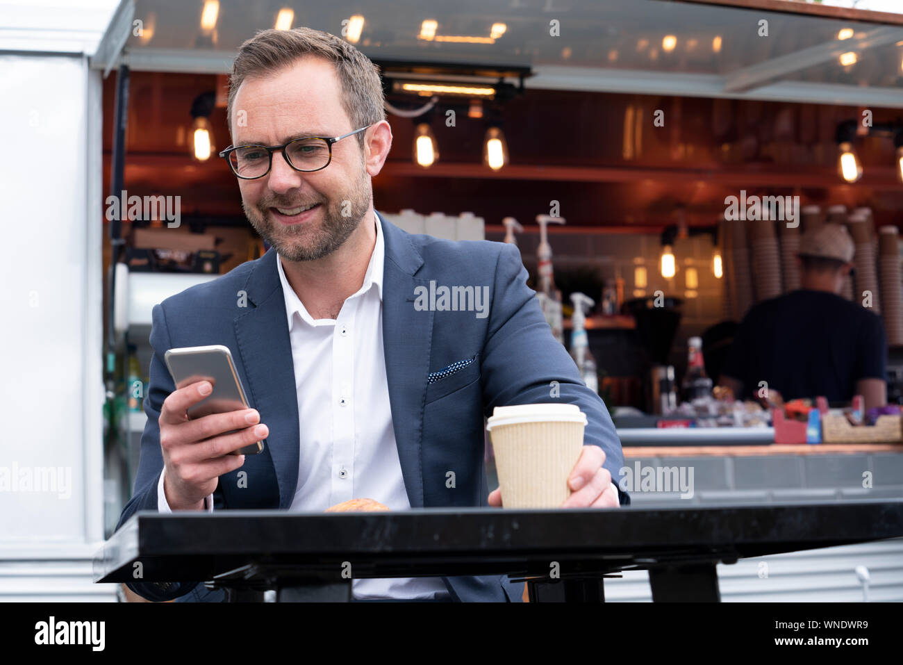 Imprenditore maturo controllo telefono cellulare seduti al Outdoor Coffee Shop Foto Stock