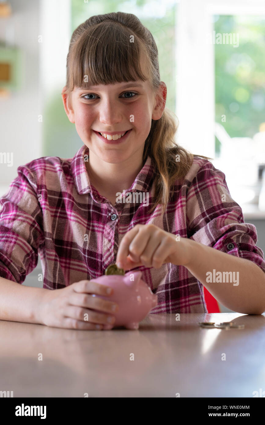 Ritratto di ragazza mettendo di monete in Piggybank a casa per mostrare il risparmio di denaro Foto Stock