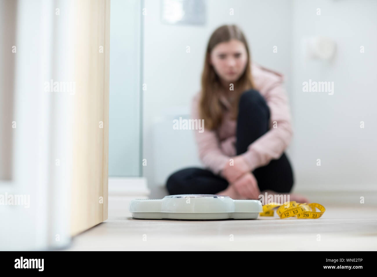 Infelice ragazza seduta nel bagno guardando le scale e il nastro di misurazione Foto Stock