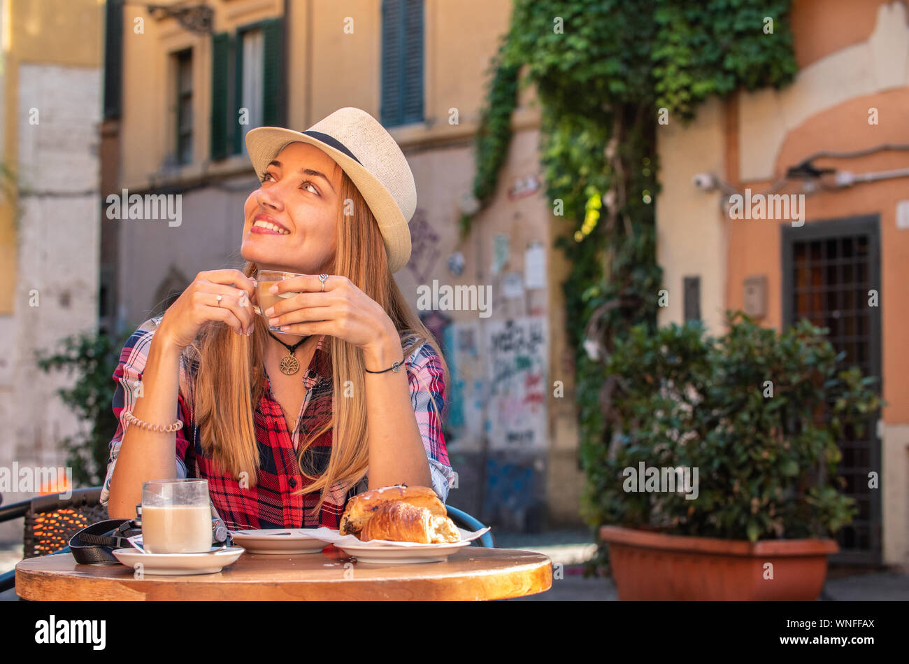 Giovane donna bionda con gli occhi blu di fare colazione nel bar in tipico stile italiano al di fuori nel quartiere storico Trastevere a Roma, Italia. Cappuccino Foto Stock
