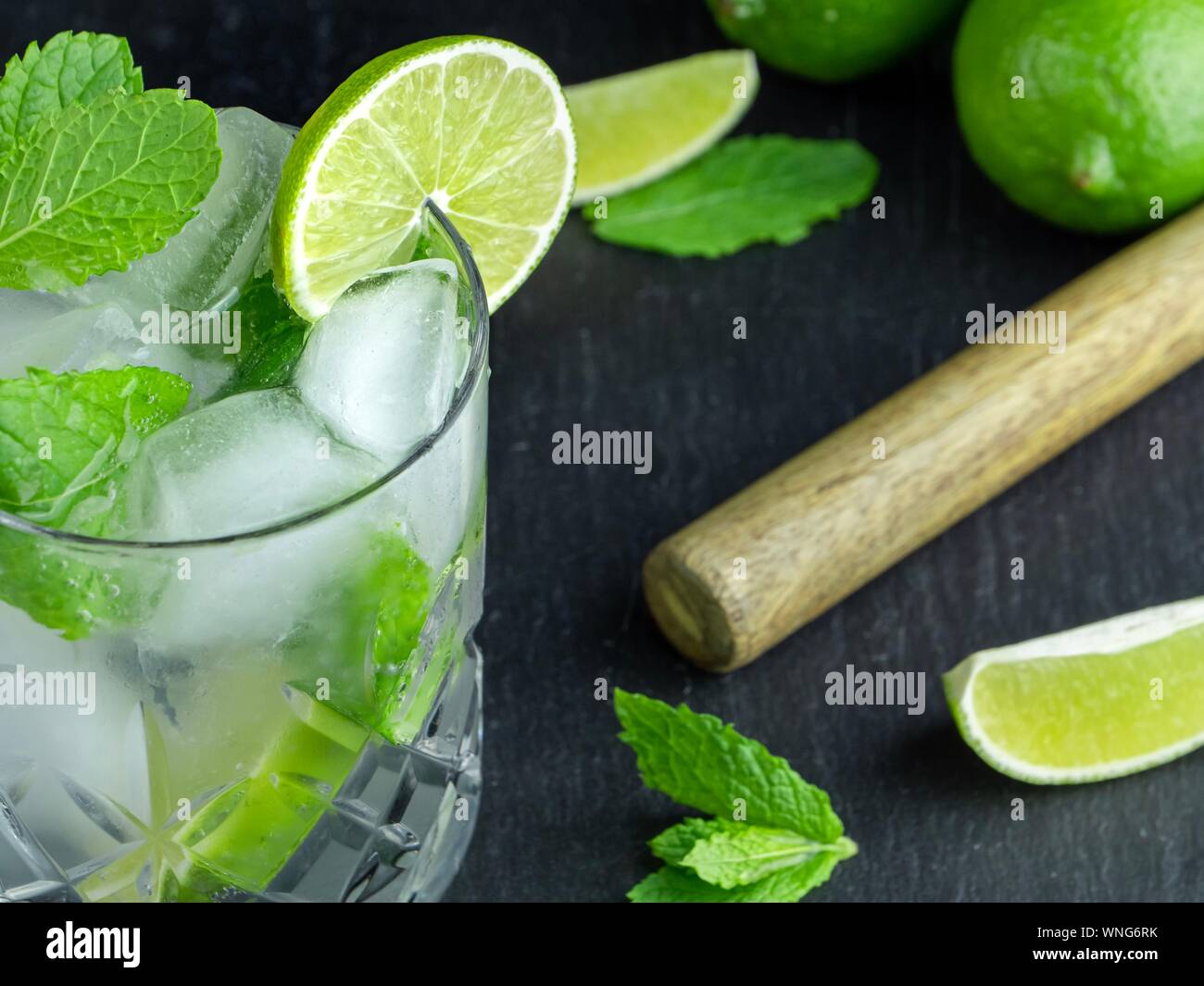 Un cocktail mojito realizzato da menta fresca e lime in un taglio di un bicchiere di vetro contro un nero ardesia sfondo Foto Stock