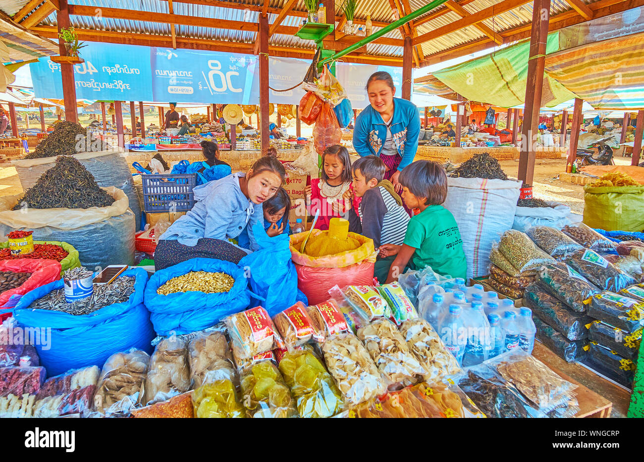 KAKKU, MYANMAR - Febbraio 20, 2018: la famiglia di agricoltori con bambini piccoli nel cibo stallo del mercato Kakku; i bambini giocano tra pacchetti con tagliatelle, ba Foto Stock