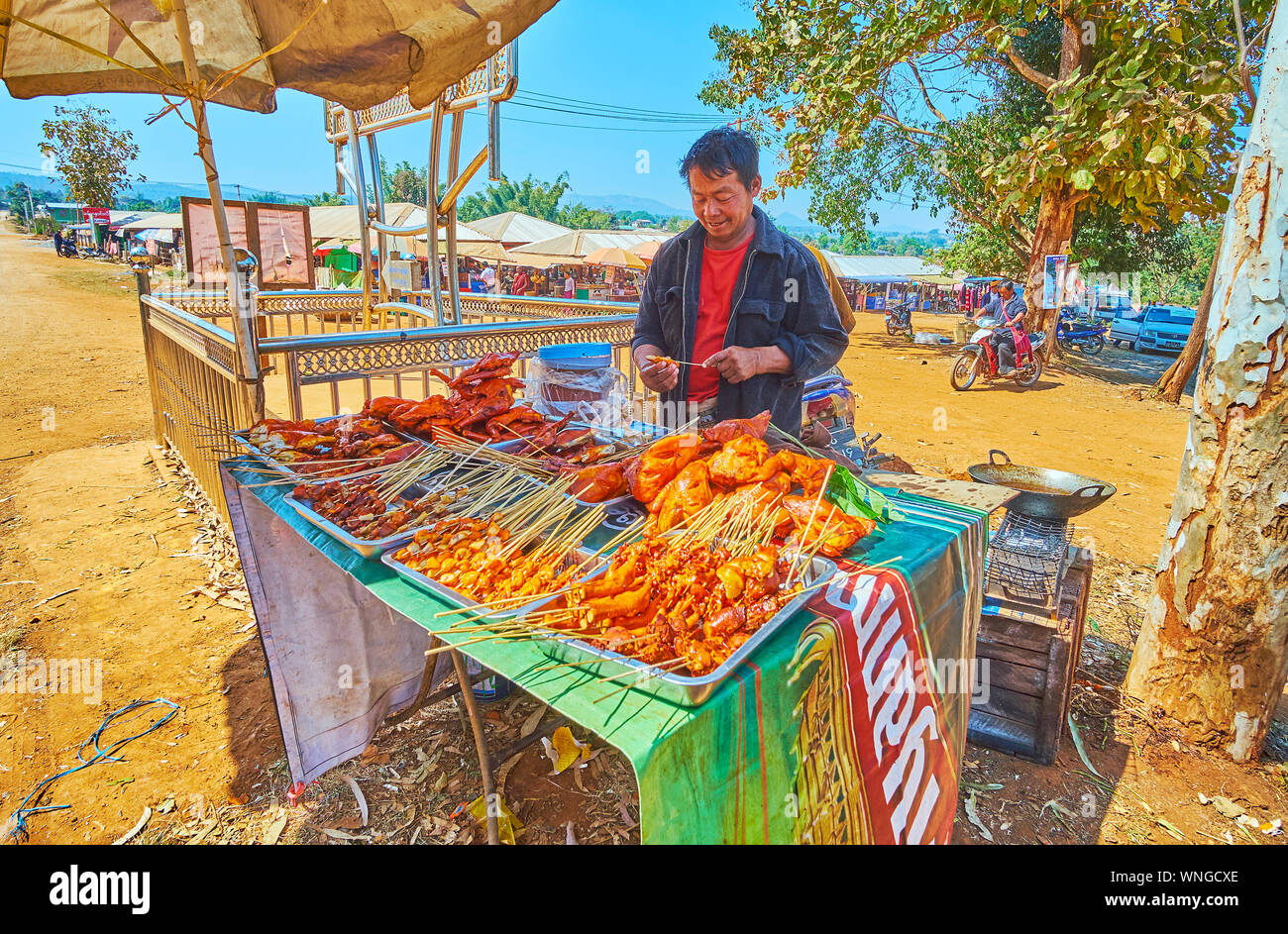 KAKKU, MYANMAR - 20 febbraio 2018: il cibo di strada fornitore offre pollo alla griglia su spiedini all'ingresso al mercato Kakku, su 20 Febbraio in Kakku. Foto Stock