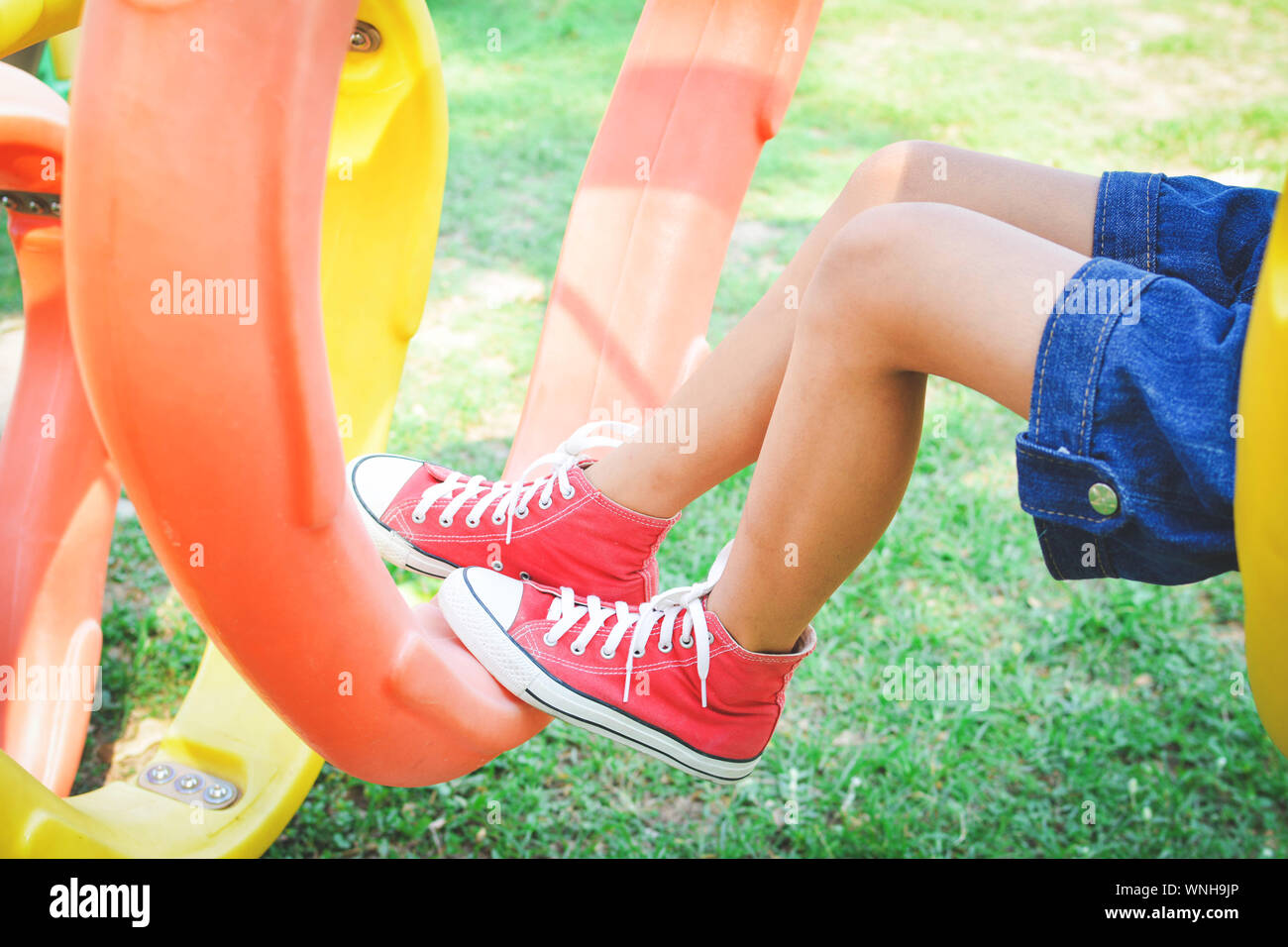 Immagine ritagliata della ragazza seduta da attrezzature per il gioco presso il parco giochi Foto Stock