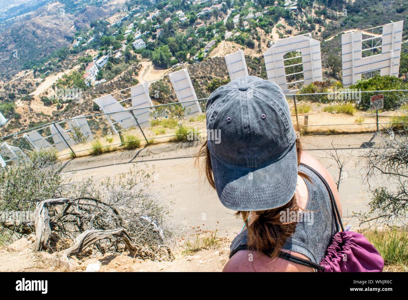 Ragazza giovane con il cappello sulla cima di una collina dietro il segno di Hollywood (giorno di estate) - Los Angeles, California, Stati Uniti d'America Foto Stock