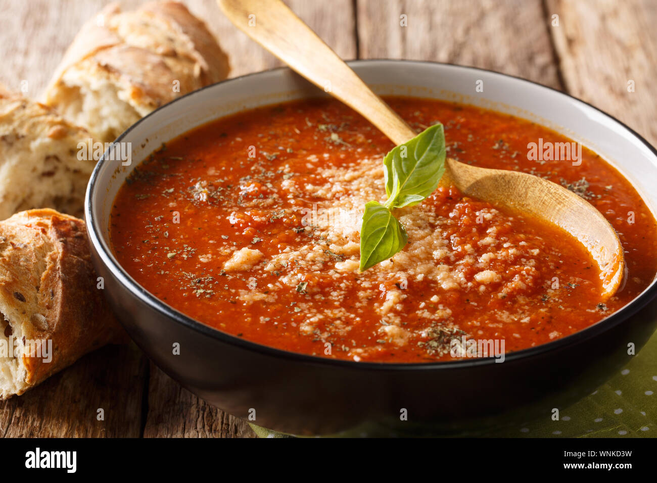 Di spessore al pomodoro e basilico minestra di crema di parmigiano close-up in una ciotola con il pane sulla tavola orizzontale. Foto Stock