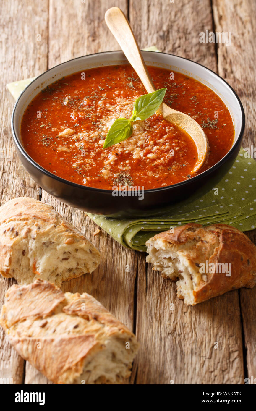 Pomodoro saporita zuppa di basilico con parmigiano close-up in una ciotola con il pane sulla tavola verticale. Foto Stock