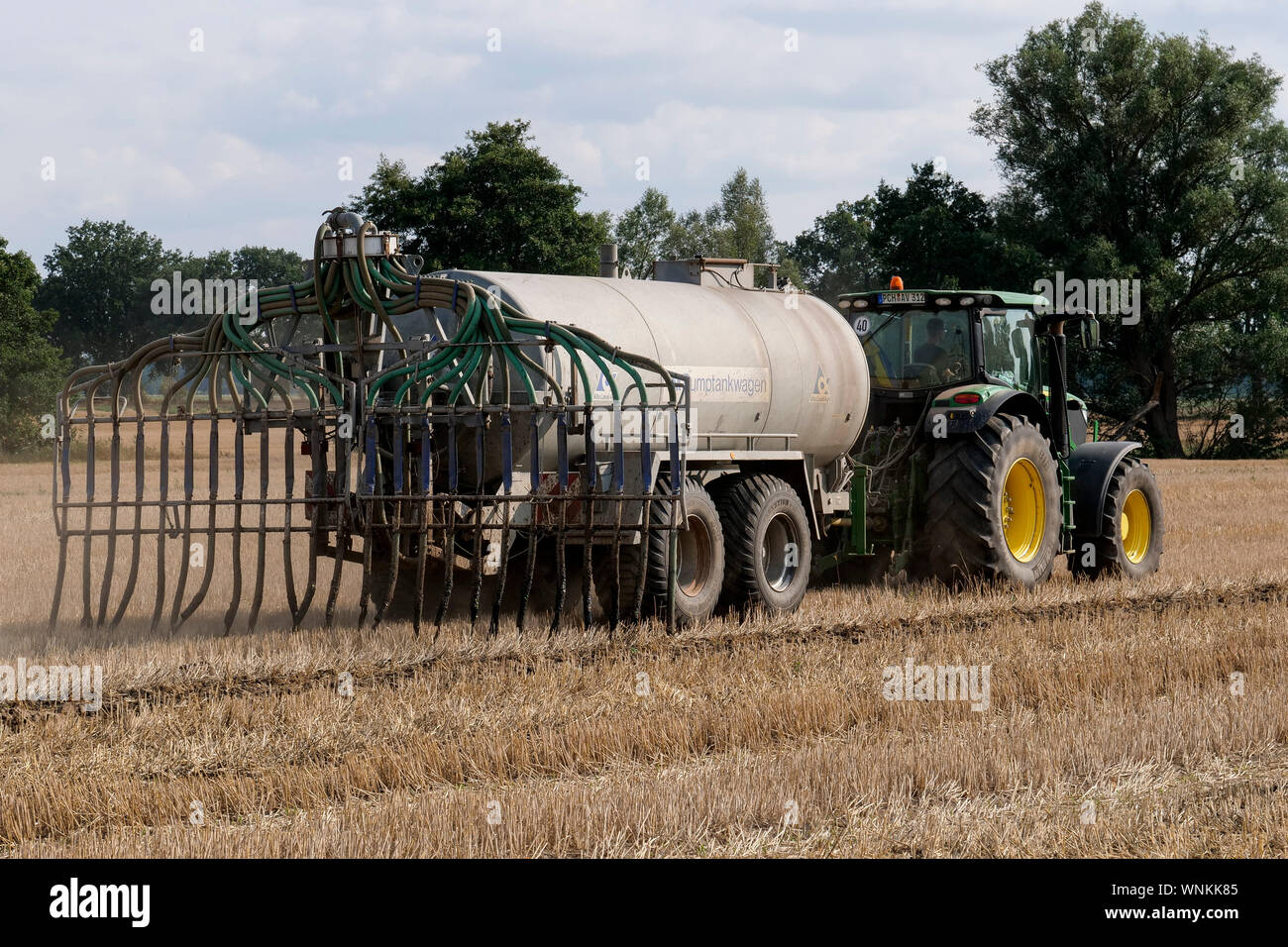 GERMANIA, agricoltura, trattore John Deere di grandi dimensioni con carro cisterna per liquame su campo, concime liquido spruzzato su campo raccolto, liquame da capannoni di maiale e vacca con ad alto contenuto di nitrati inquinamenti acque sotterranee / DEUTSCHLAND, Mecklenburg Vorpommern, Traktor mit Guellewagen bringt Guelle auf ein Stoppelfeld aus, Zu viele nitrato belasten das Grundwasser Foto Stock