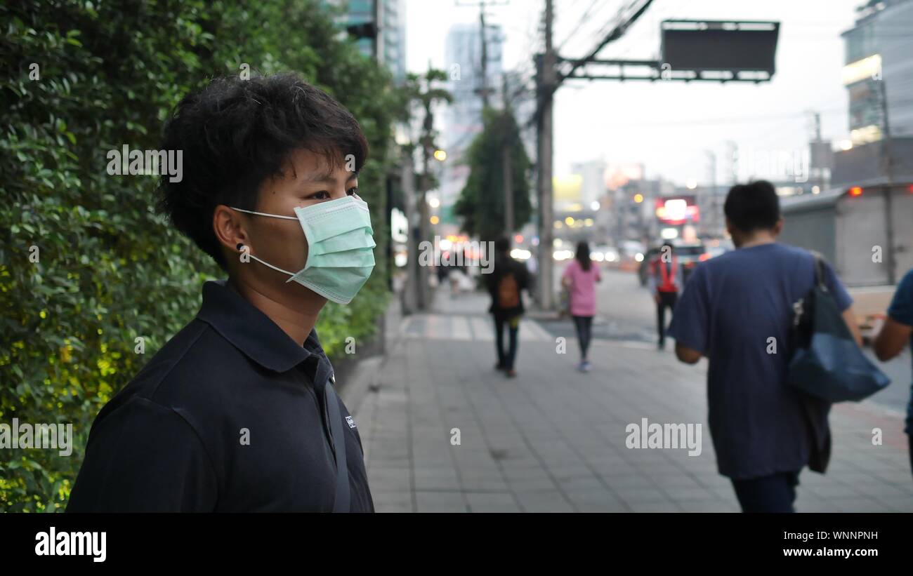 Uomo che indossa la maschera di inquinamento in piedi sul marciapiede in città Foto Stock