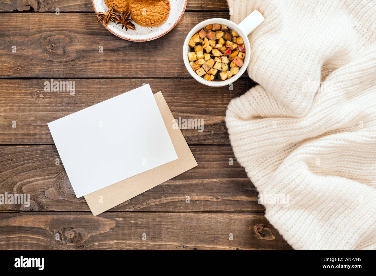 In autunno o inverno flatlay composizione con lana bianca plaid, carta bianca card mockup, Busta, tazza di tè caldo, biscotti. Accogliente casa di accoglienza, hygge vacanze Foto Stock