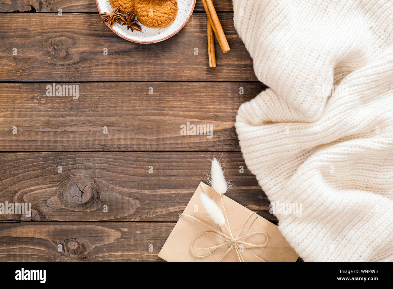 In autunno o inverno flatlay composizione con lana bianca plaid, crft busta di carta, bastoncini di cannella, cookie, fiori secchi. Accogliente casa di accoglienza, hygge concetto. Foto Stock