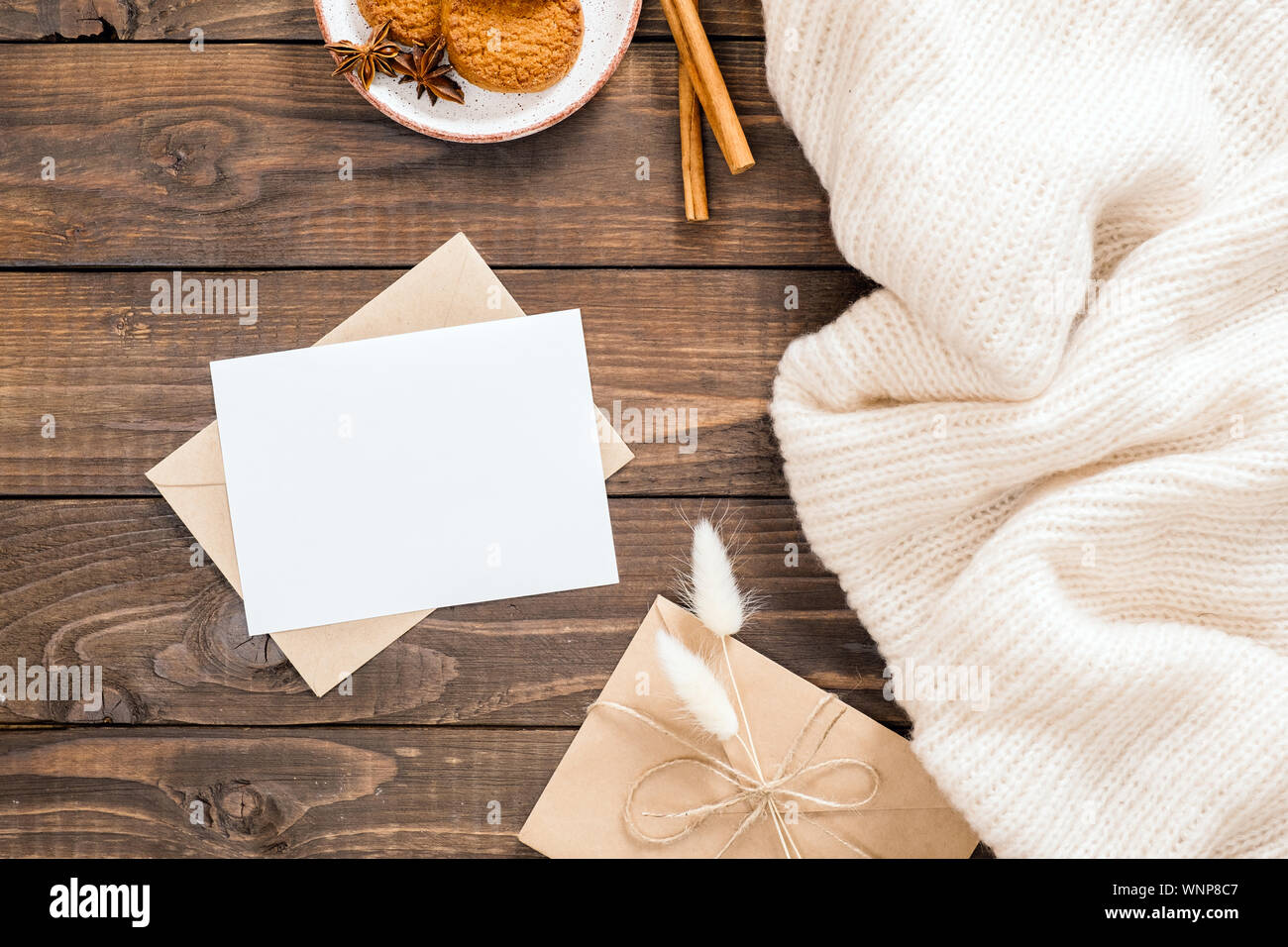 In autunno o inverno flatlay composizione con lana bianca plaid, carta bianca card mockup, Busta, bastoncini di cannella, cookie, fiori secchi. Accogliente casa di accoglienza Foto Stock