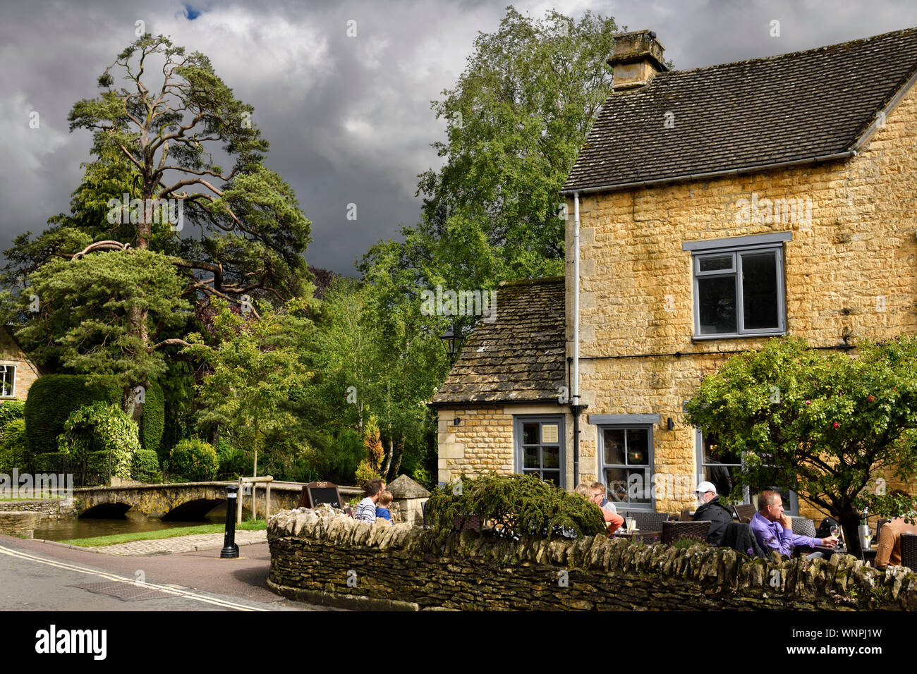 Il Croft pub terrazza esterna in sun con pino e passerella sul Fiume Windrush a Bourton-on-the-acqua Gloucestershire in Inghilterra Foto Stock