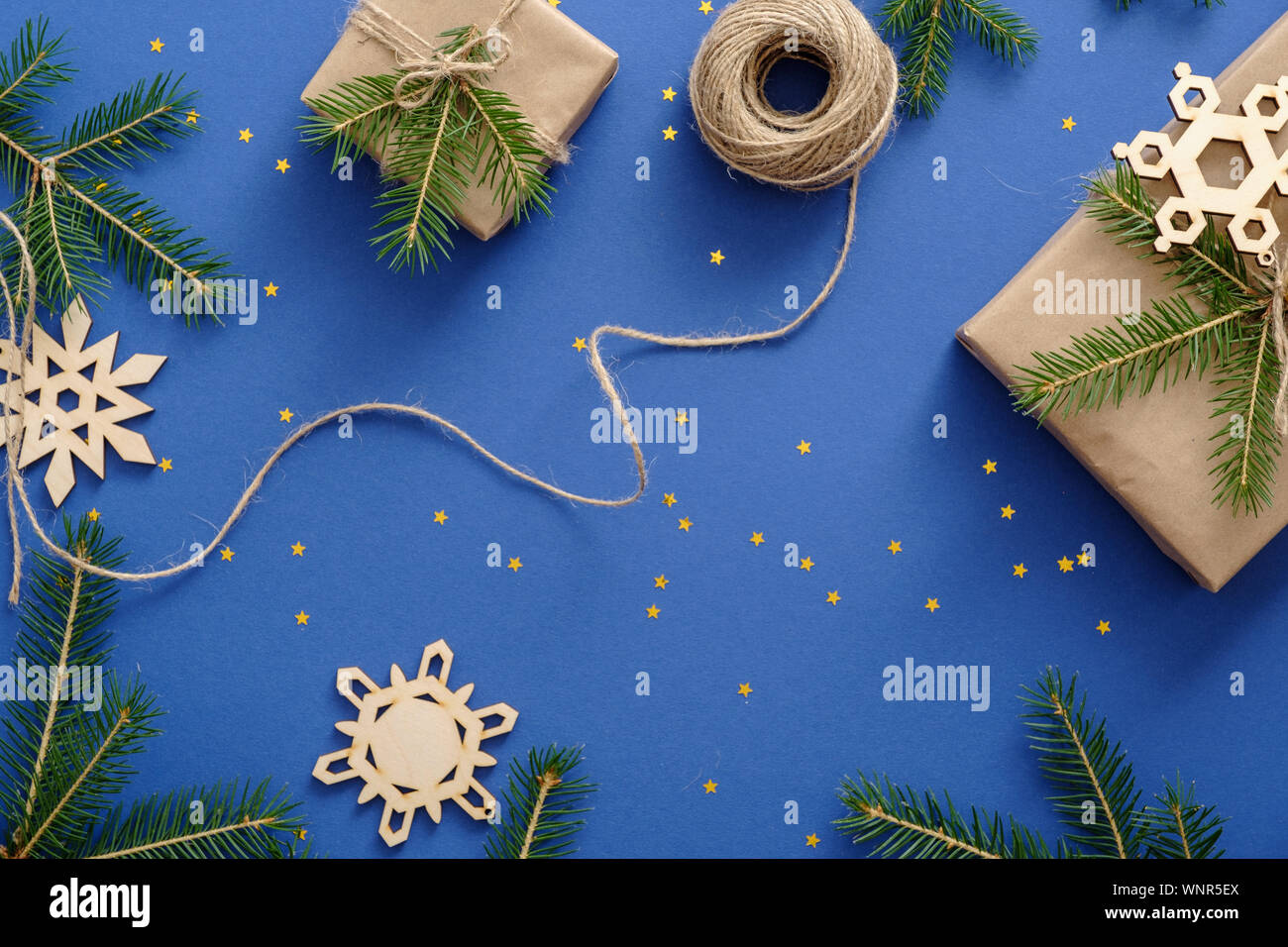 Decorazioni di Natale, in legno realizzati a mano i fiocchi di neve, Xmas regali avvolti in carta kraft, Abete rami, coriandoli su sfondo blu. Natale, inverno Foto Stock