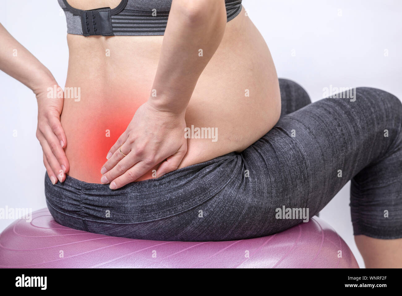 Dolori e. Attiva donna incinta esercitarsi nel centro fitness in sala yoga. La giovane madre prevedente tenendo le mani sul retro e sitts al fitness Foto Stock