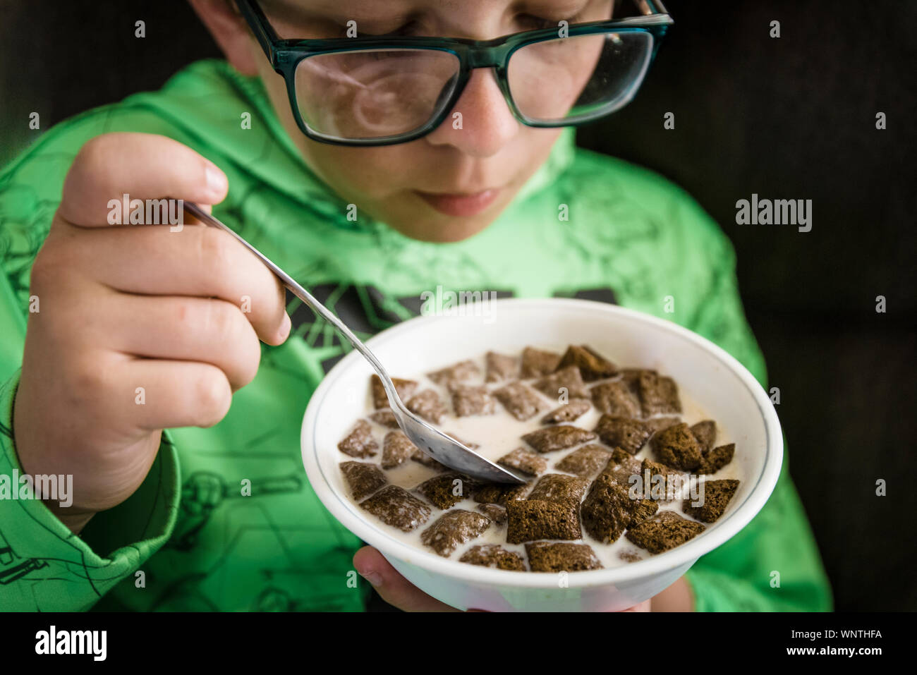 Ragazzo di mangiare il suo cioccolato cereali da una vaschetta di colore bianco per la prima colazione. Foto Stock