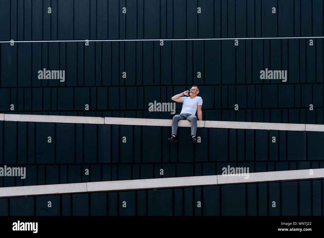 Ritratto di maturo uomo barbuto al telefono seduto su un muro esterno Foto Stock
