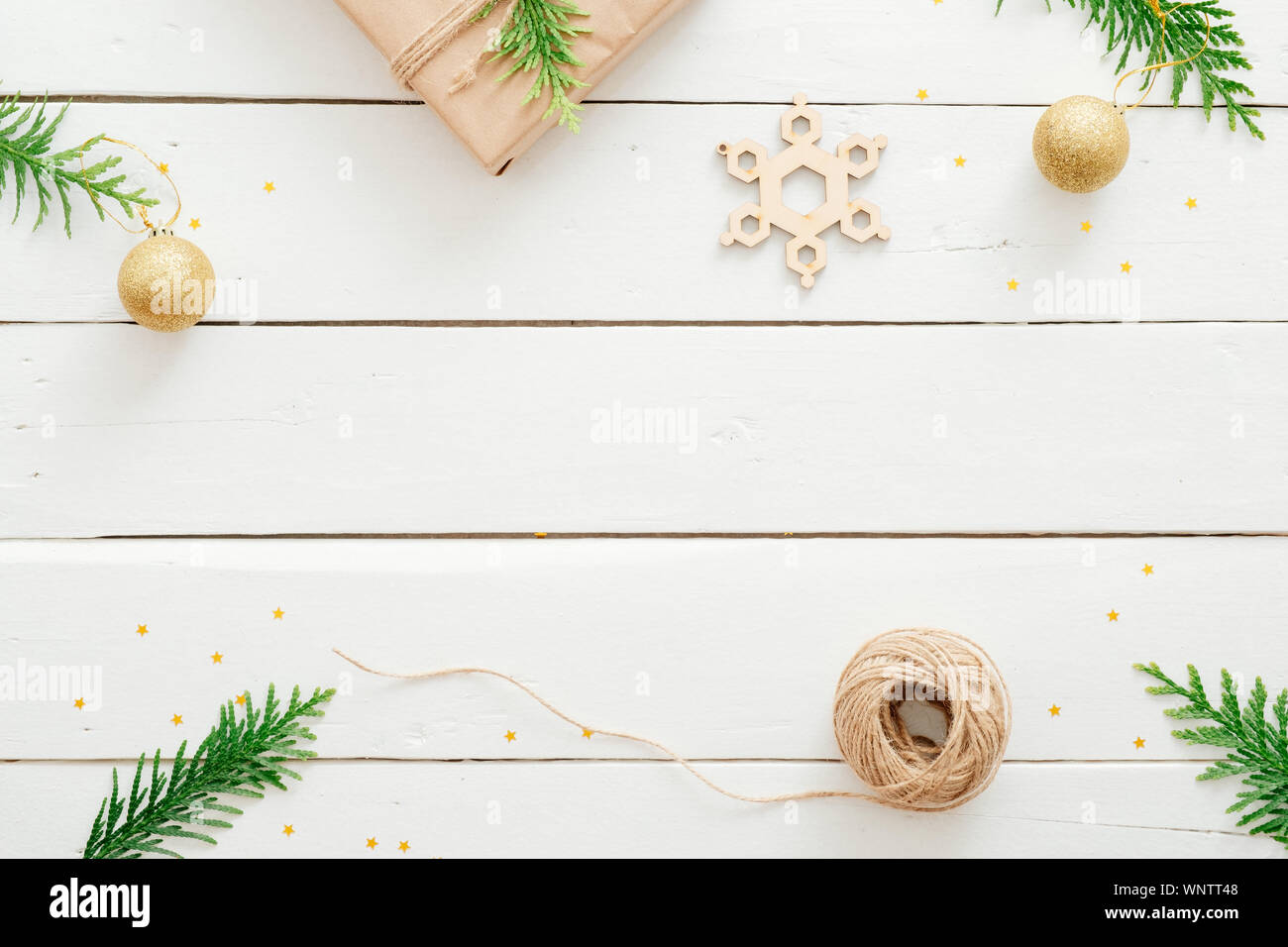 Natale stile flatlay composizione. Abete rami, di dono, di spago, palline dorate, fatta a mano il simbolo del fiocco di neve sul bianco in legno scrivania. Sfondo di natale. Appartamento Foto Stock
