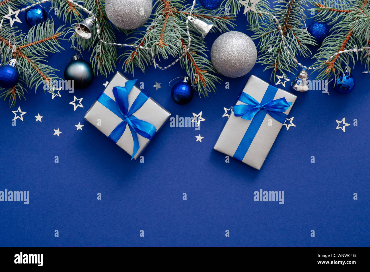 Moderne decorazioni di Natale, Abete rami, argento baubles, confezioni regalo con nastro bow, coriandoli su sfondo blu scuro. Buon Natale e Hap Foto Stock