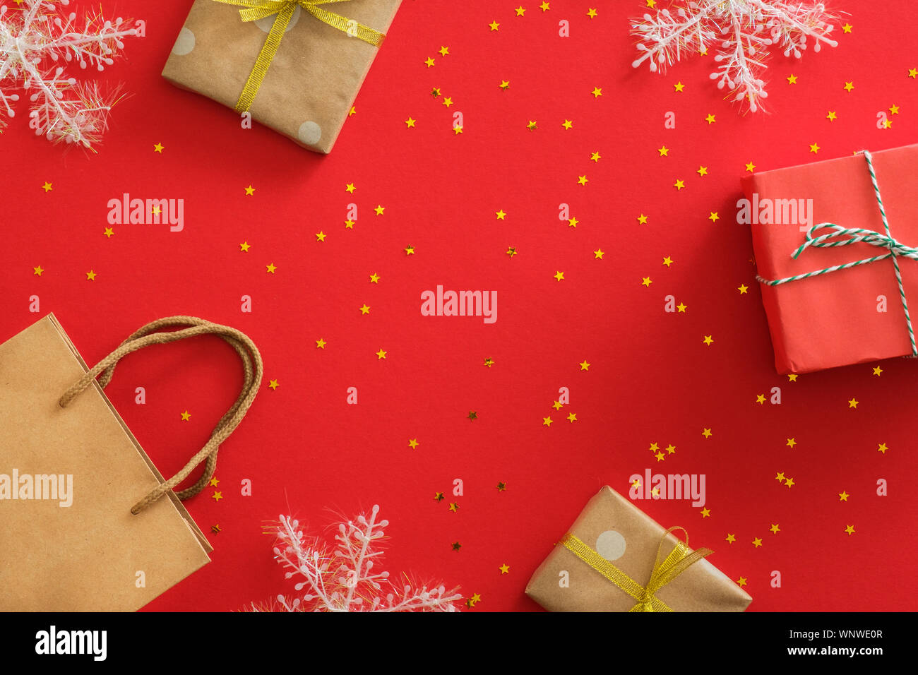 Anno nuovo Natale regali avvolti carta craft, fiocchi di neve, decorazioni, glitter golden coriandoli su sfondo rosso. Vacanze di Natale celebrazione del concetto. Foto Stock