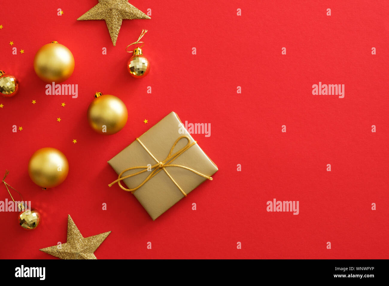 Natale decorazioni in oro su sfondo rosso con copia spazio. Piatto dorato laici confezione regalo, baubles, stelle scintillanti coriandoli. Poster di Natale mockup, Foto Stock