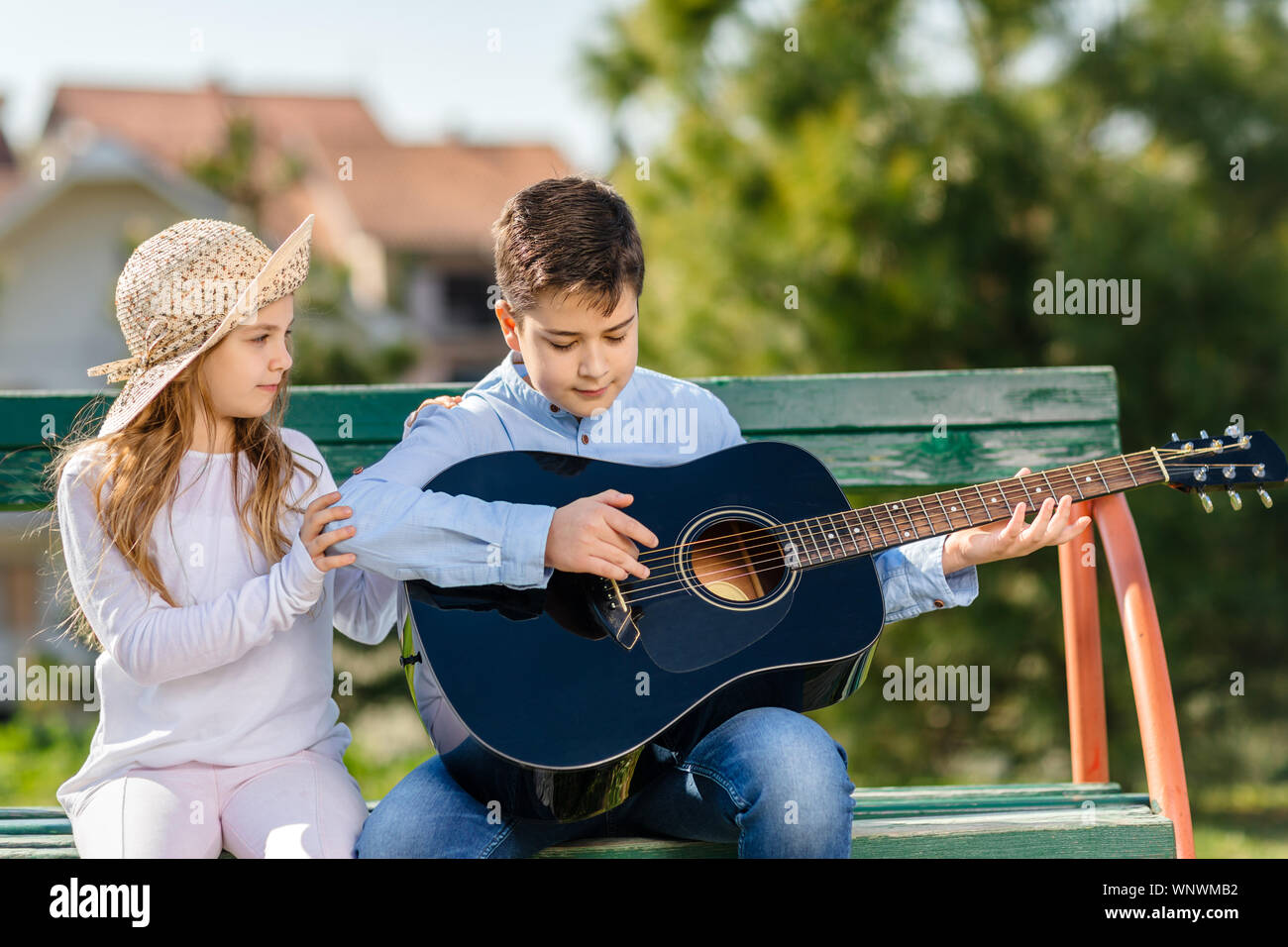 Giovane ragazza e ragazzo con la chitarra seduto al banco nel parco. I bambini amano. Foto Stock