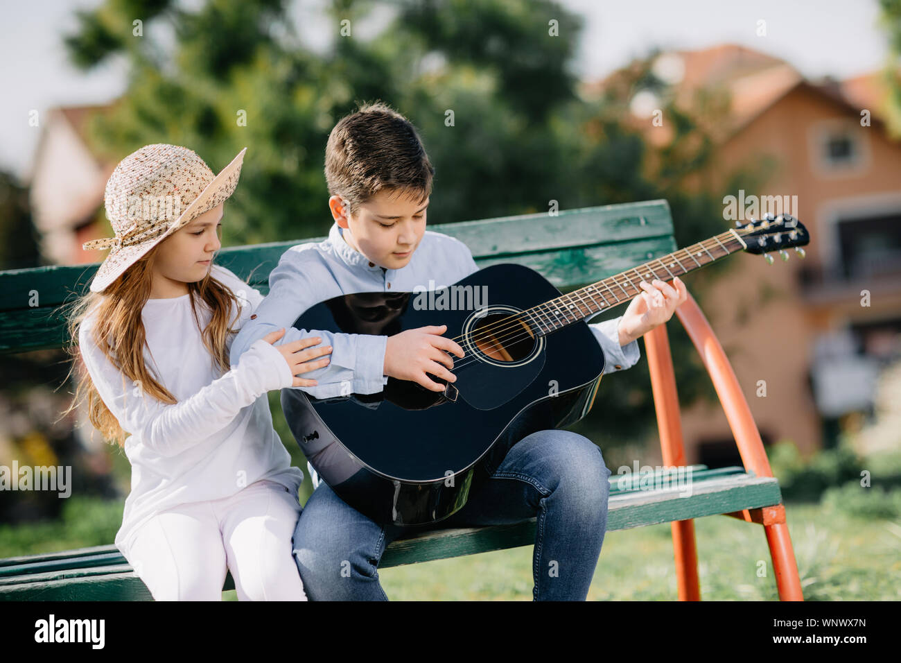 Giovane ragazza e ragazzo con la chitarra seduto al banco nel parco. I bambini amano. Foto Stock