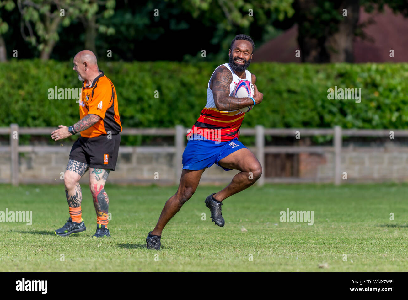 Amatoriale Fijiano giocatore di rugby sprint lontano da arbitro di Norfolk, palla in mano e grande sorriso sul suo volto. Foto Stock