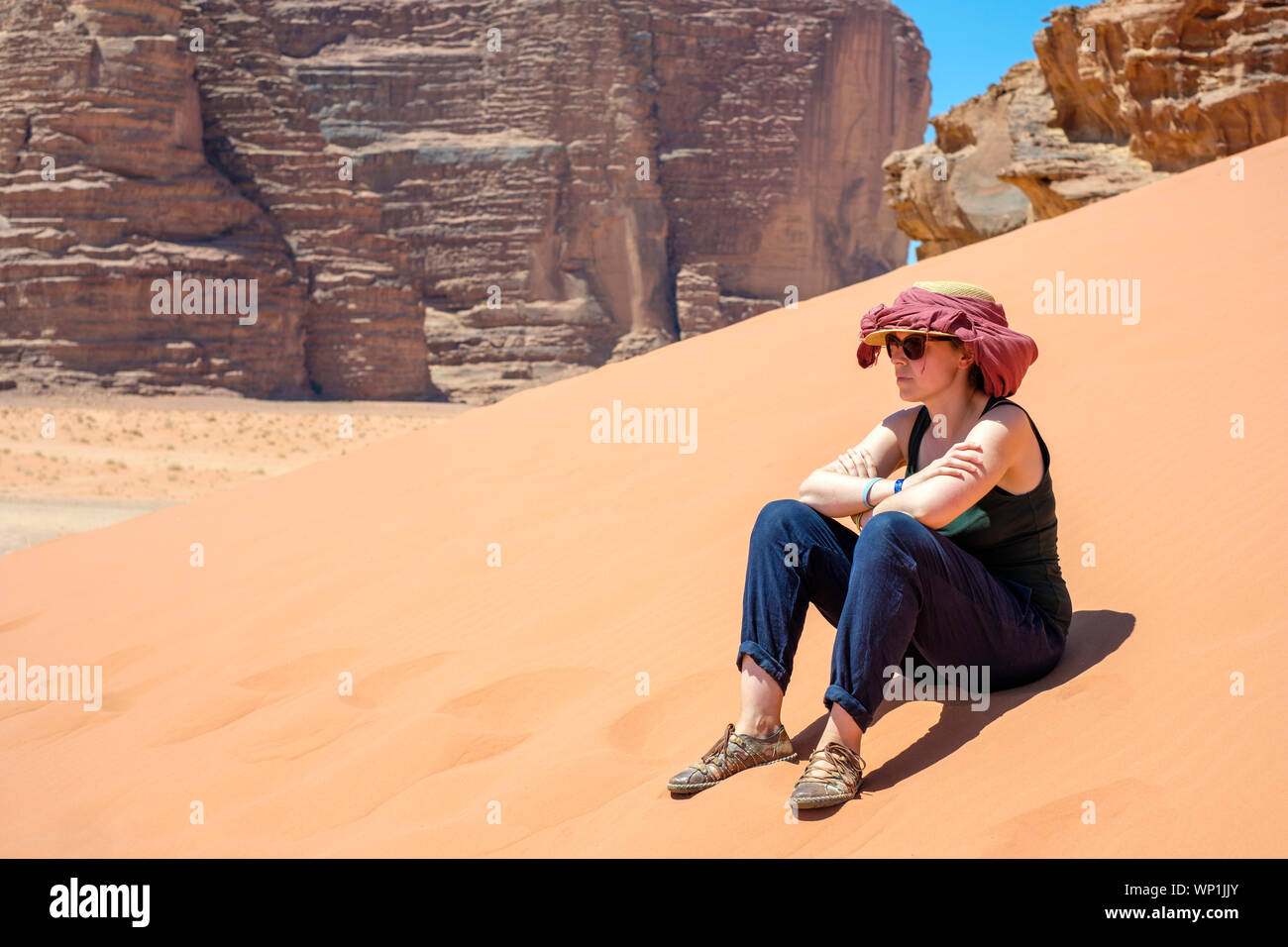 Giordania, Governatorato di Aqaba, Wadi Rum. Wadi Rum Area Protetta, Sito Patrimonio Mondiale dell'UNESCO. Un turista si siede su una duna di sabbia nel sole caldo. (MR) Foto Stock