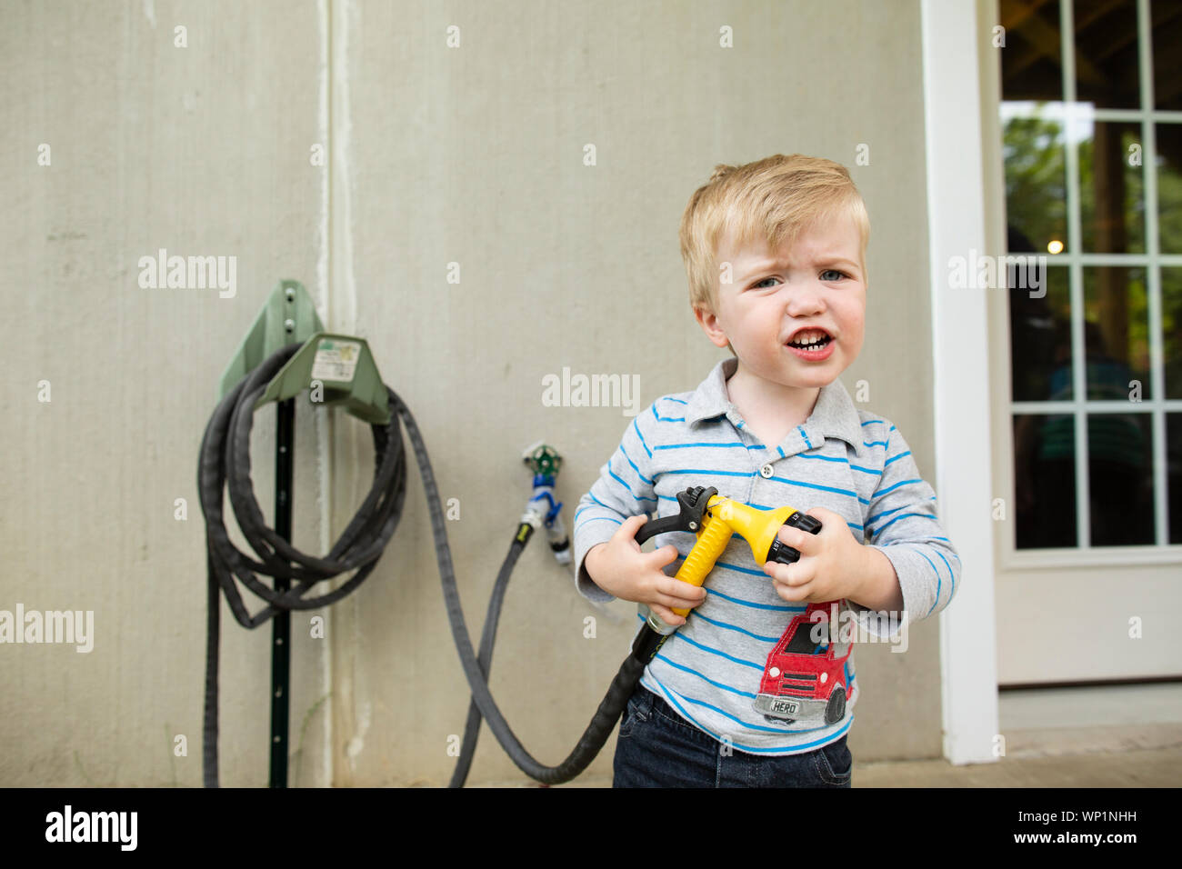 Carino biondo toddler boy appare frustrato mantenendo al di fuori del tubo flessibile Foto Stock