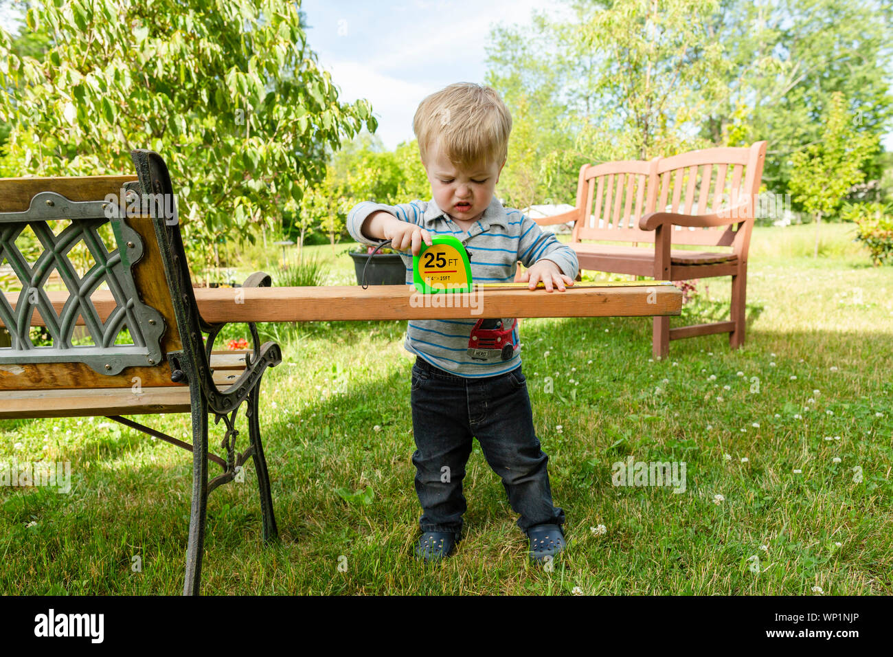 Il Toddler boy appare frustrato durante la misurazione di legno all'aperto Foto Stock