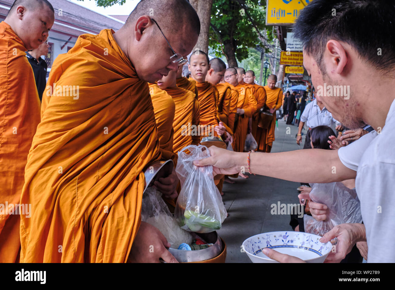 I monaci buddisti sulla loro la mattina presto alms round accodamento per ricevere elemosine da adoratori sperando di ottenere il merito spirituale (tham manna); Bangkok, Thailandia Foto Stock