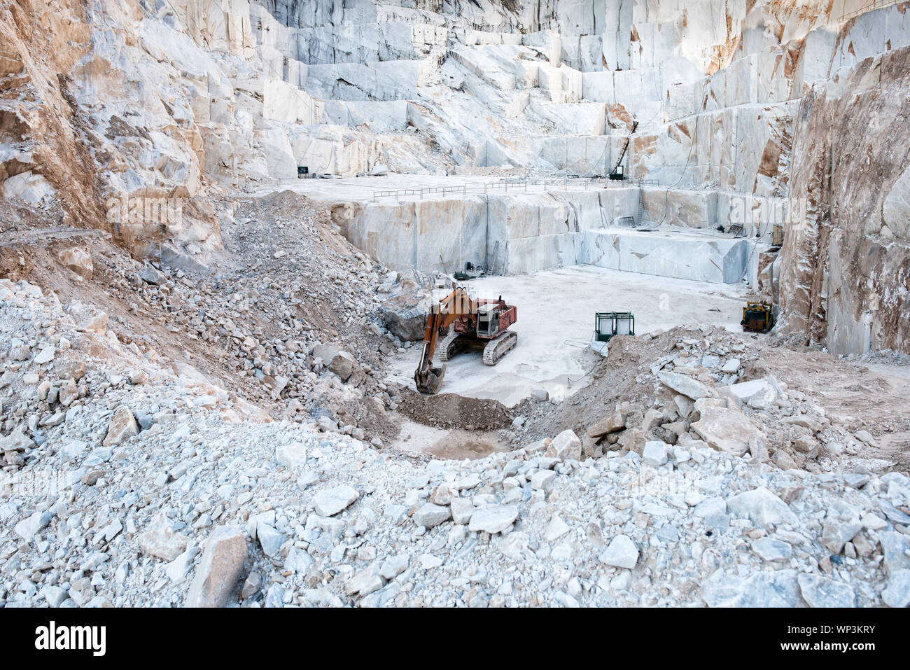 Escavatore o all'interno di scavo un open cast mining pit per il marmo bianco di Carrara che mostra i grandi blocchi di pietra tagliata dal versante della montagna in Toscana, Italia Foto Stock