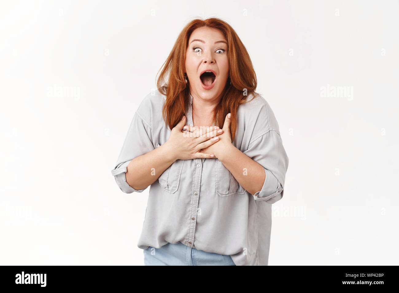 Sorpreso eccitato sconvolto di mezza età senza parole redhead donna guardano storditi mascella caduta di tenere le mani cuore impresso vincere lotteria inaspettato grande novità, mo Foto Stock